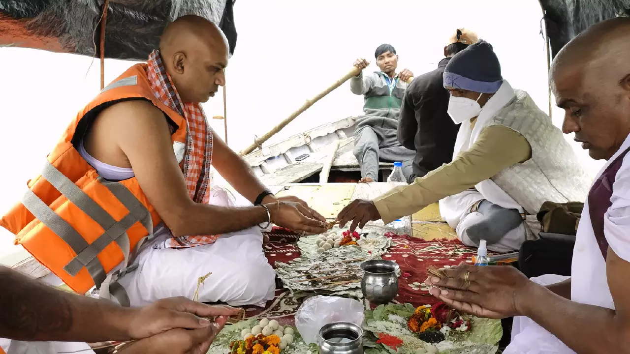 Men participate in a traditional ritual aboard a boat. Dressed in customary attire, with one wearing an orange life vest, they handle offerings like flowers and food placed on leaves. Another man rows the boat in the background during what appears to be a riverside ceremony - Pitrupaksha is in autumn