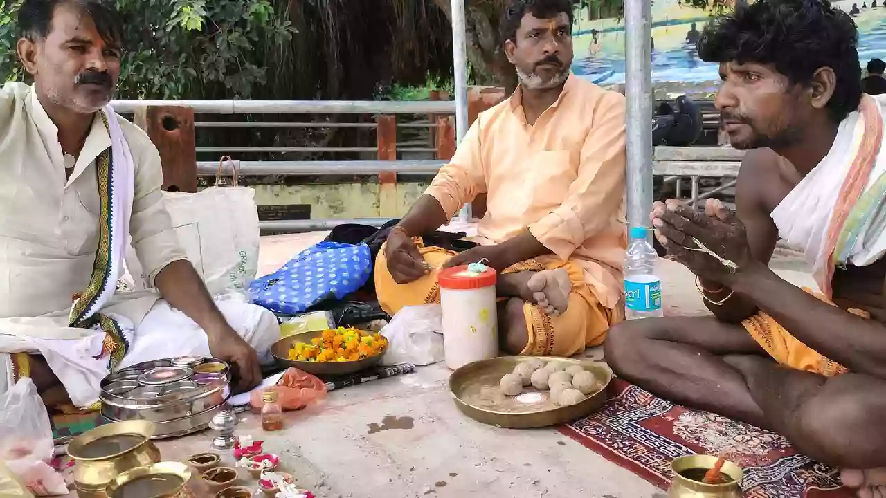 Picture of three man sitting on the ground near the ghat and from three, two are pandits and one man do rituals for there ancestor's on the time of Pitrupaksha Shraddha Tithis