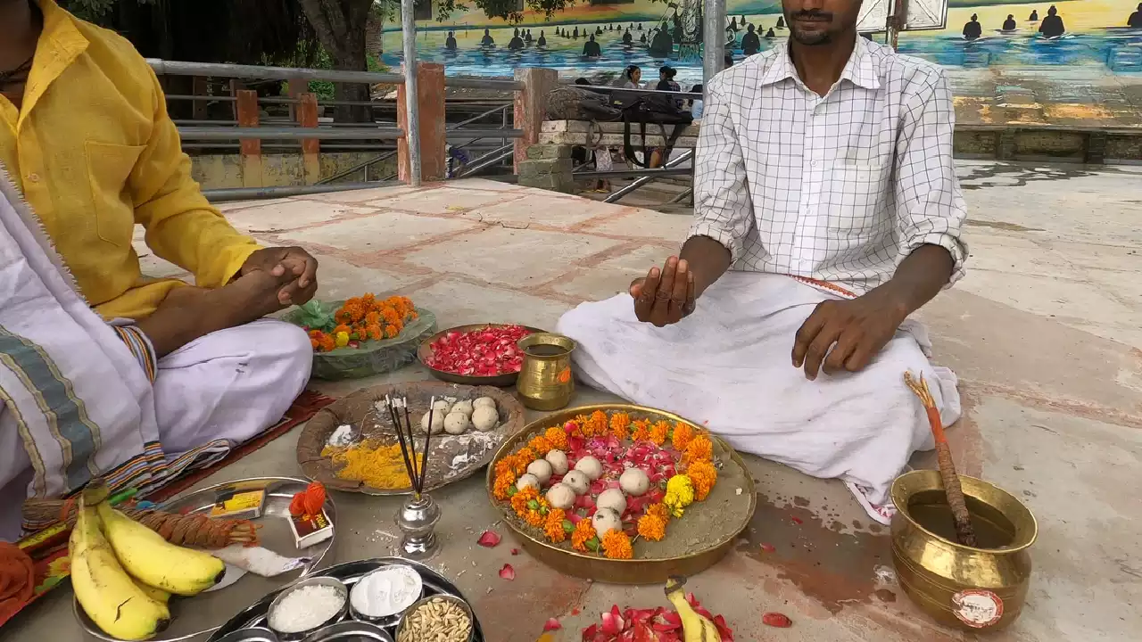 Two men sit facing each other for Shradh ritual. Offerings include Pindas, flowers, altar, fruits.