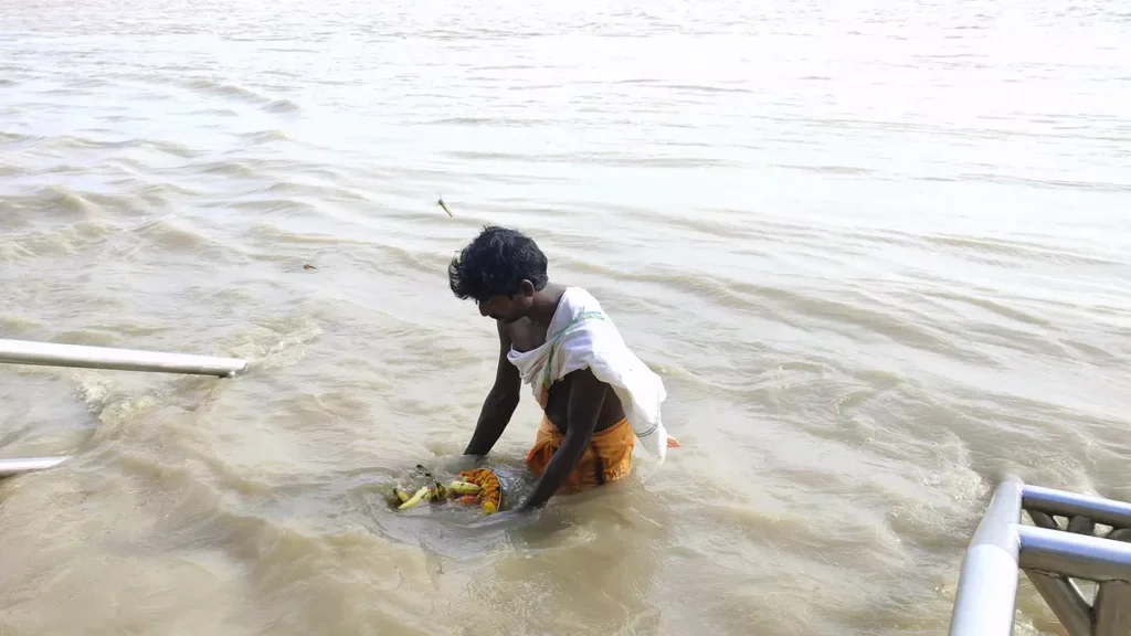 Man performing tarpan ritual in river, offering bananas & flowers on plate. Pitru Paksha observance-Simple Tarpan mantras